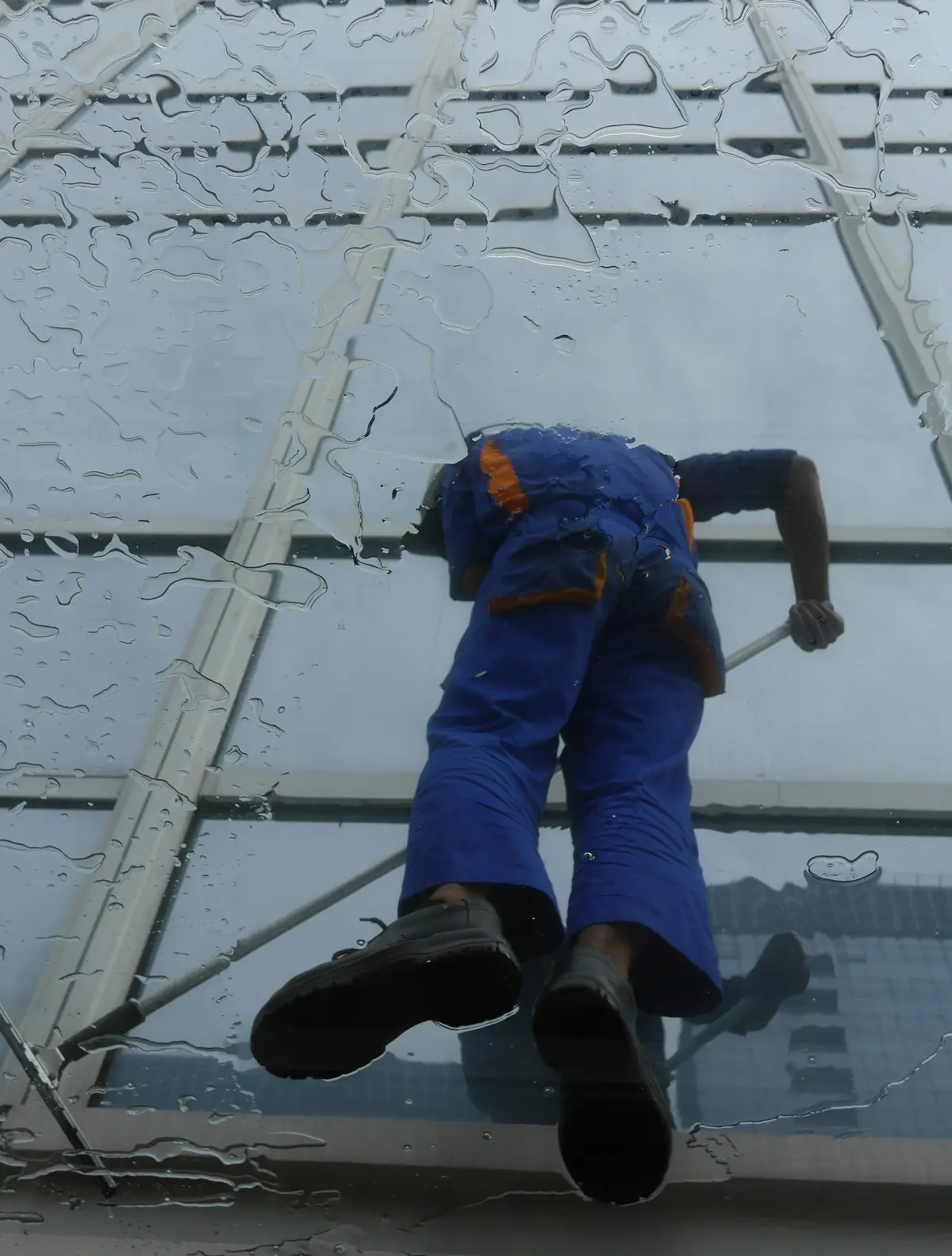 Glazenwasser aan het werk op een glazen gevel, gezien door het natte glas